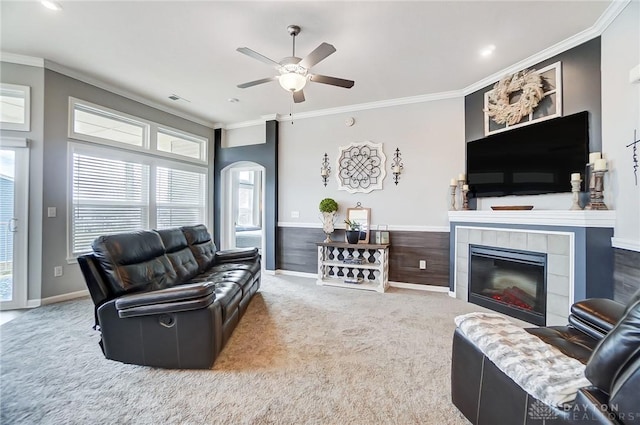 carpeted living room featuring a tiled fireplace, ornamental molding, and ceiling fan