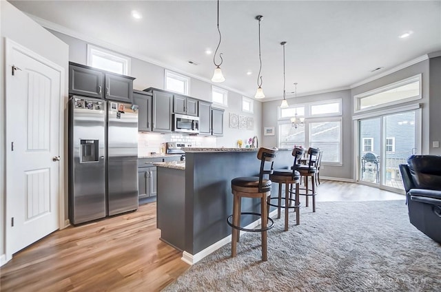 kitchen with pendant lighting, appliances with stainless steel finishes, light stone counters, ornamental molding, and a kitchen bar