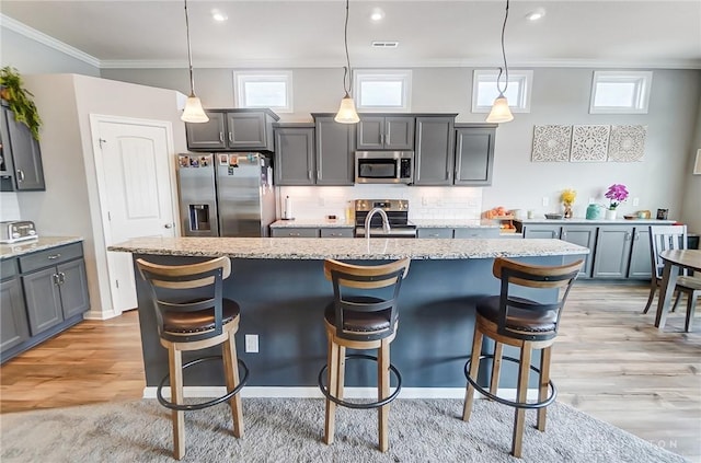 kitchen featuring decorative light fixtures, stainless steel appliances, an island with sink, and a kitchen bar