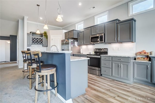 kitchen featuring hanging light fixtures, crown molding, a center island with sink, and appliances with stainless steel finishes