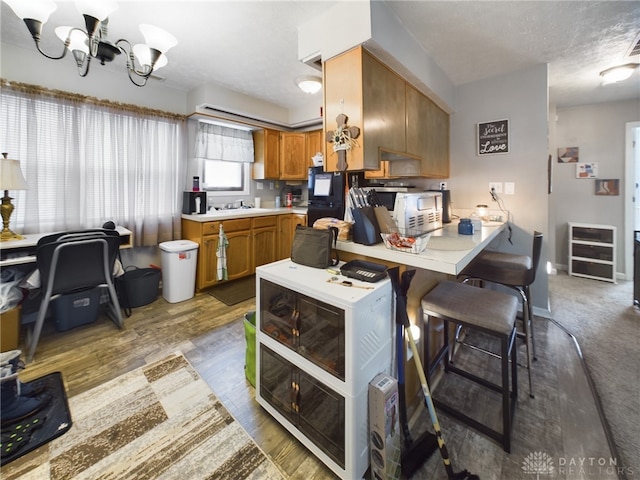 kitchen with hardwood / wood-style floors, a chandelier, a kitchen breakfast bar, kitchen peninsula, and a textured ceiling