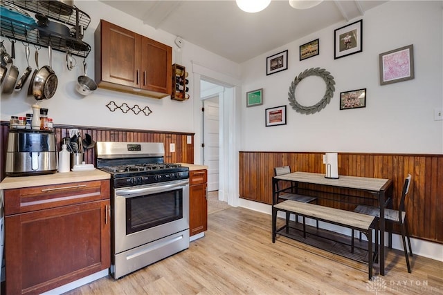 kitchen with wooden walls, light hardwood / wood-style floors, and stainless steel gas range oven