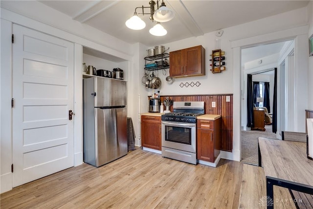 kitchen with hanging light fixtures, beam ceiling, stainless steel appliances, and light wood-type flooring