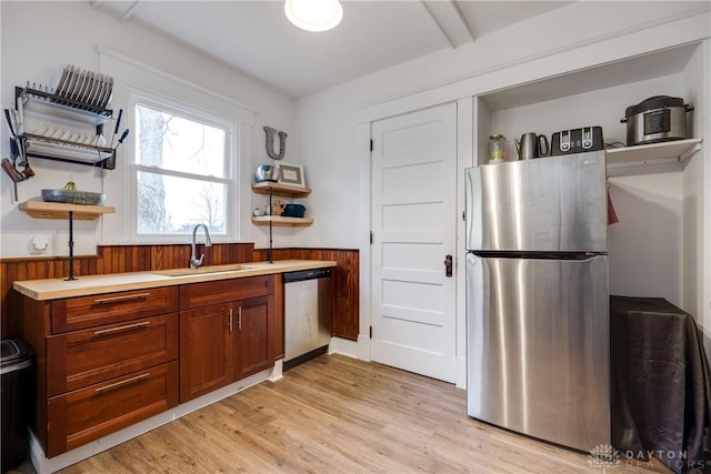 kitchen featuring sink, light wood-type flooring, wood walls, and appliances with stainless steel finishes