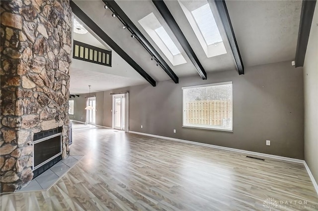 unfurnished living room featuring lofted ceiling with skylight, track lighting, a fireplace, and light hardwood / wood-style floors