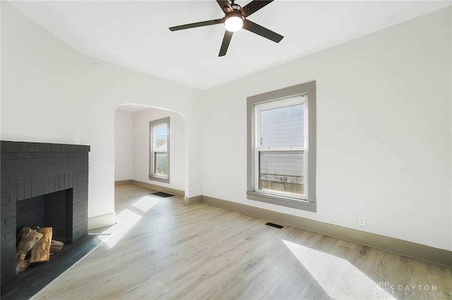 living room with ceiling fan, a brick fireplace, and light wood-type flooring