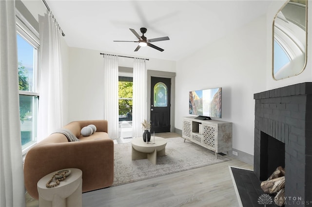 living room with ceiling fan, a brick fireplace, and light wood-type flooring