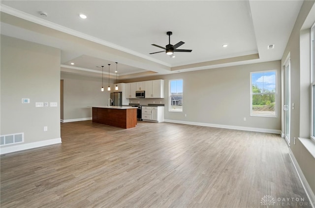 1507 Kingsgate, Springfield, OH 45502 - unfurnished living room featuring a tray ceiling, crown molding, a ceiling fan, light wood-style floors, and healthy amount of natural light