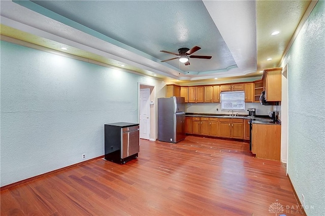 kitchen with dark wood-type flooring, stainless steel refrigerator, a tray ceiling, ceiling fan, and stove