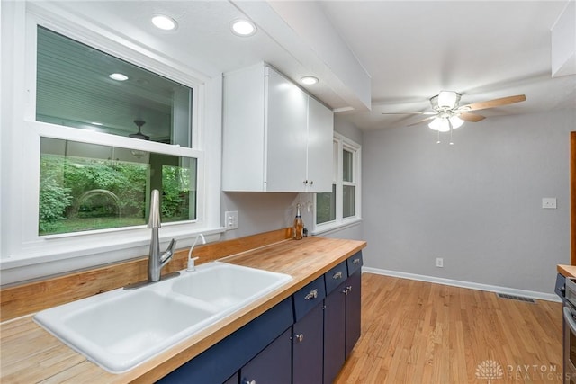 kitchen with butcher block countertops, sink, white cabinets, and ceiling fan