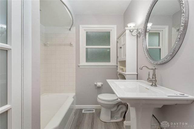 bathroom featuring tiled shower / bath combo, hardwood / wood-style floors, and toilet