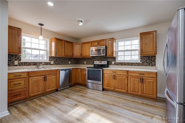 kitchen with appliances with stainless steel finishes, decorative light fixtures, sink, and light wood-type flooring