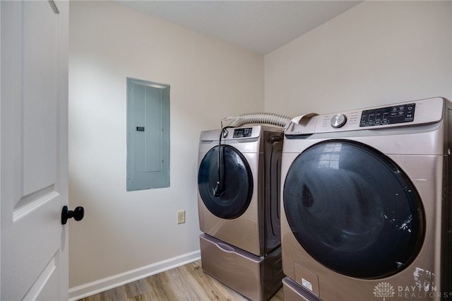 clothes washing area with light wood-type flooring, electric panel, and washer and clothes dryer