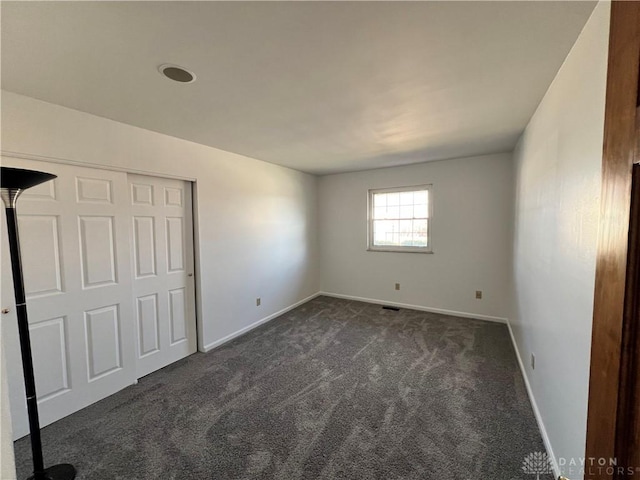 unfurnished bedroom with dark colored carpet and a closet