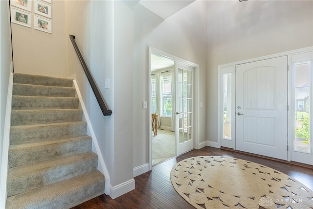 entrance foyer featuring dark wood-type flooring, a wealth of natural light, and a towering ceiling