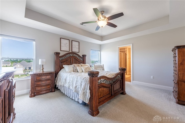 bedroom with light colored carpet, a tray ceiling, and multiple windows