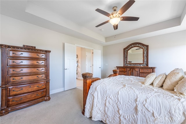 bedroom with light colored carpet, a raised ceiling, and ceiling fan