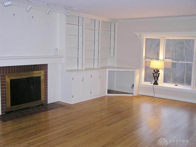 unfurnished living room featuring a brick fireplace, crown molding, hardwood / wood-style floors, and rail lighting