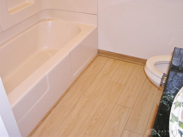 bathroom with wood-type flooring, a bath, and toilet