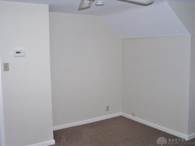 spare room featuring vaulted ceiling, ceiling fan, and dark colored carpet