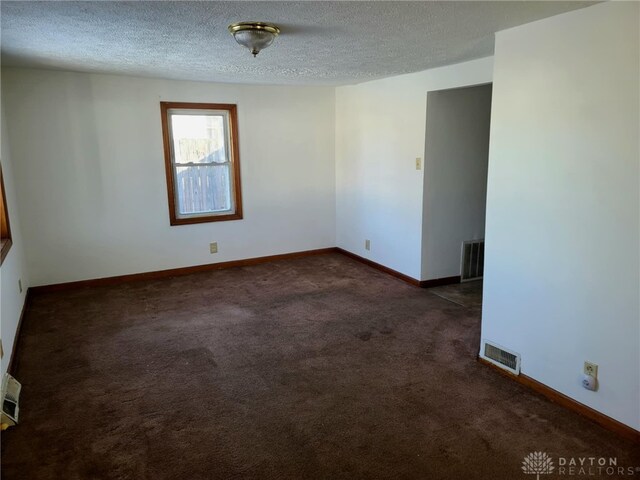 empty room featuring a textured ceiling and dark carpet