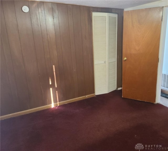 unfurnished bedroom featuring a closet, wood walls, and dark colored carpet