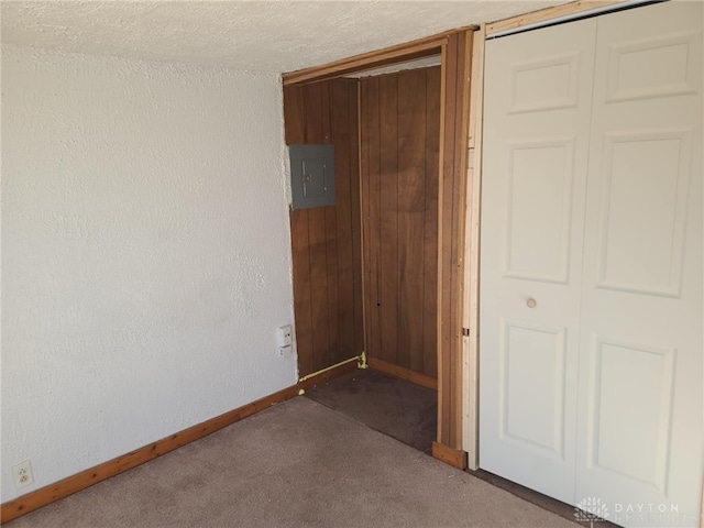 unfurnished bedroom featuring wooden walls, carpet flooring, electric panel, a textured ceiling, and a closet