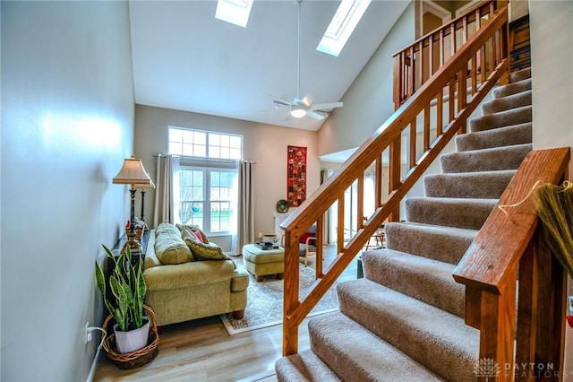 stairs featuring hardwood / wood-style flooring, ceiling fan, a skylight, and high vaulted ceiling