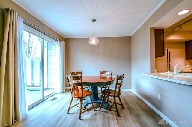 dining room featuring hardwood / wood-style flooring, crown molding, rail lighting, and sink