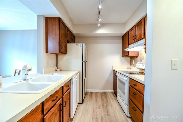 kitchen with rail lighting, sink, light wood-type flooring, decorative backsplash, and white appliances