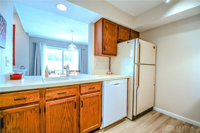 kitchen with white dishwasher, sink, hanging light fixtures, and light wood-type flooring