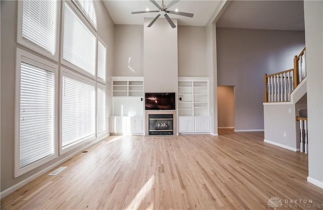 unfurnished living room featuring a high ceiling, ceiling fan, light wood-type flooring, and a fireplace