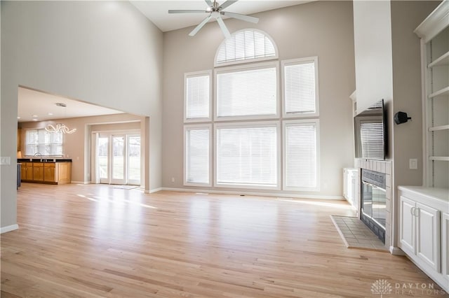 unfurnished living room with a fireplace, light hardwood / wood-style floors, ceiling fan, and a high ceiling