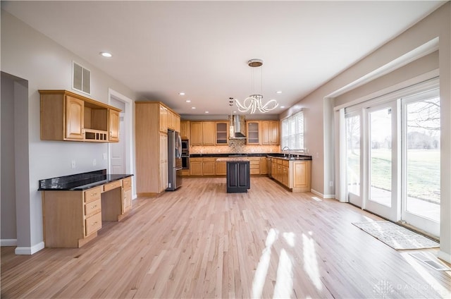 kitchen with appliances with stainless steel finishes, hanging light fixtures, tasteful backsplash, wall chimney exhaust hood, and light wood-type flooring