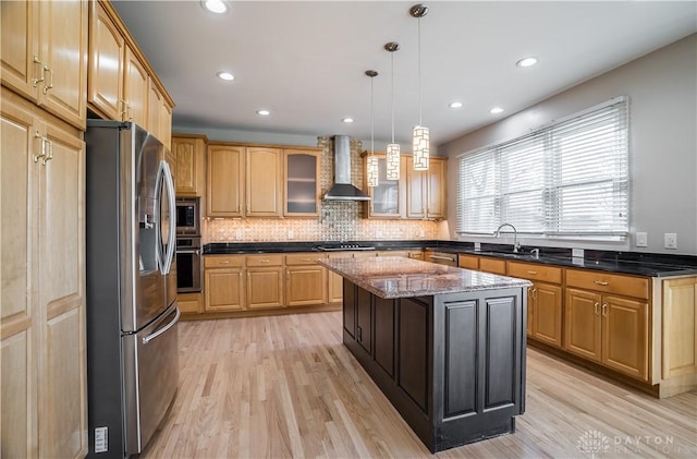 kitchen with wall chimney range hood, dark stone countertops, hanging light fixtures, stainless steel appliances, and a kitchen island