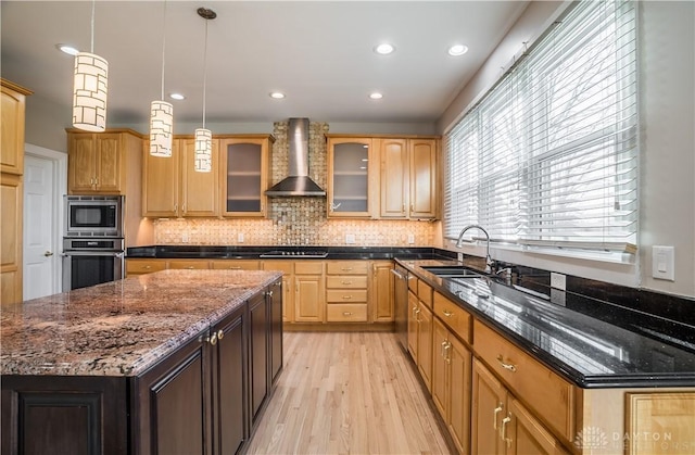 kitchen featuring appliances with stainless steel finishes, sink, dark stone counters, and wall chimney range hood