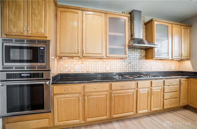 kitchen featuring backsplash, light hardwood / wood-style flooring, stainless steel appliances, and wall chimney exhaust hood