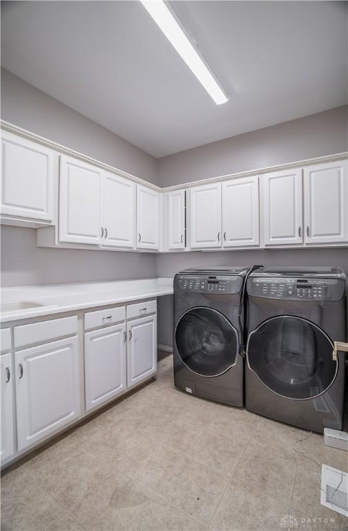 clothes washing area featuring separate washer and dryer, sink, and cabinets