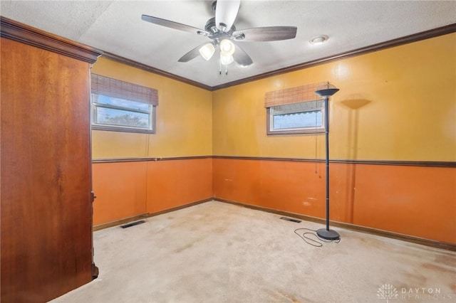 carpeted spare room featuring ceiling fan, crown molding, a textured ceiling, and a healthy amount of sunlight