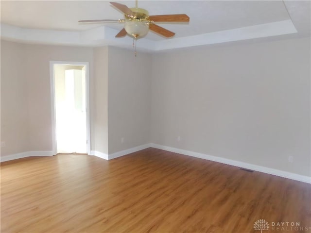 unfurnished room with hardwood / wood-style flooring, ceiling fan, and a tray ceiling