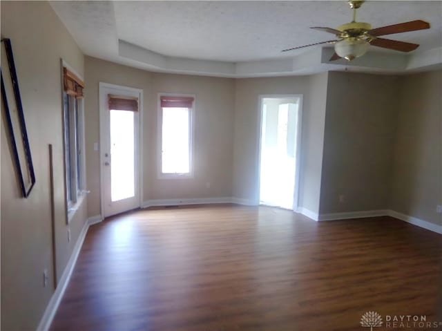 unfurnished room with dark hardwood / wood-style floors, a raised ceiling, and ceiling fan