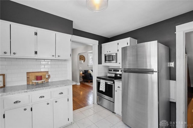 kitchen featuring white cabinetry, light tile patterned floors, stainless steel appliances, light stone countertops, and decorative backsplash