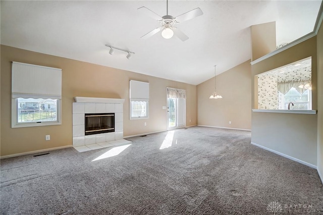 unfurnished living room featuring lofted ceiling, ceiling fan, a tiled fireplace, track lighting, and light carpet