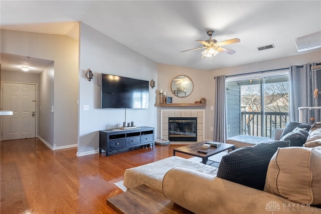 living room featuring ceiling fan, lofted ceiling, a tiled fireplace, and light hardwood / wood-style flooring