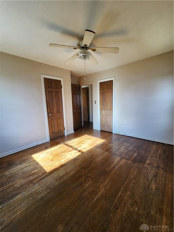 unfurnished bedroom with ceiling fan, dark hardwood / wood-style flooring, and two closets