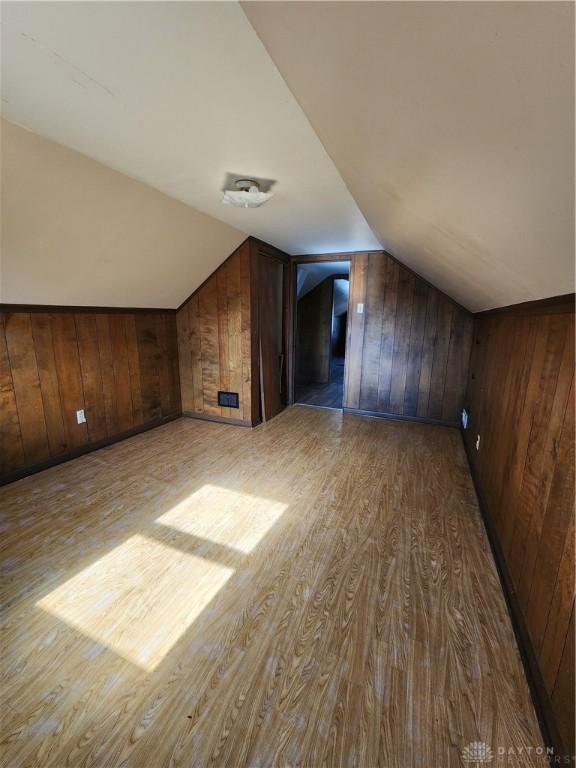 additional living space featuring lofted ceiling, wooden walls, and light wood-type flooring