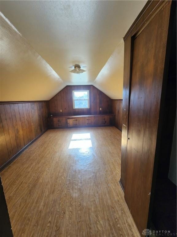 bonus room featuring lofted ceiling, a textured ceiling, light hardwood / wood-style flooring, and wood walls