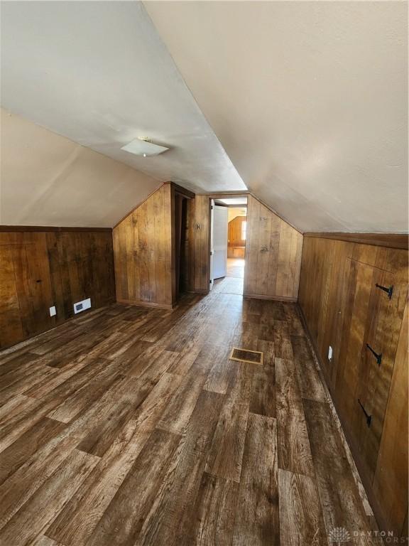 bonus room featuring dark wood-type flooring, lofted ceiling, and wooden walls