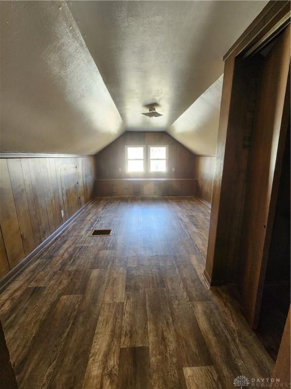 bonus room featuring lofted ceiling, dark wood-type flooring, wooden walls, and a textured ceiling