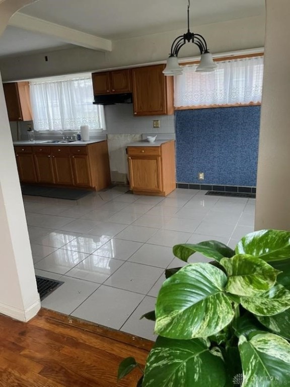 kitchen with pendant lighting, beamed ceiling, sink, and light tile patterned floors